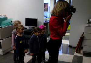 Pani fotograf wykonuje zdjęcie klientowi, a dzieci obserwują jej pracę.